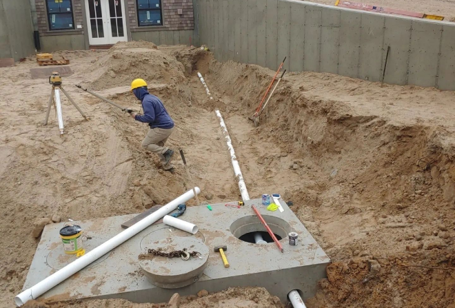 A man in blue shirt and yellow hard hat digging hole.