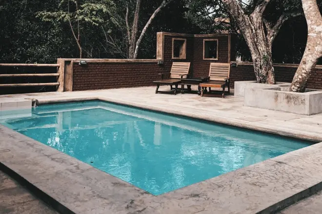 A pool with two chairs and trees in the background.