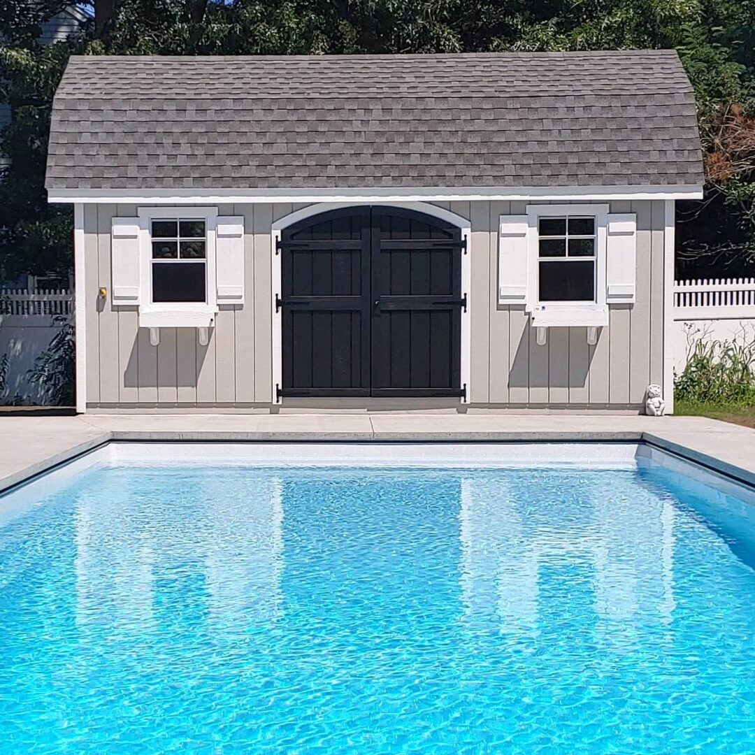 A pool house with shutters and a blue swimming pool.